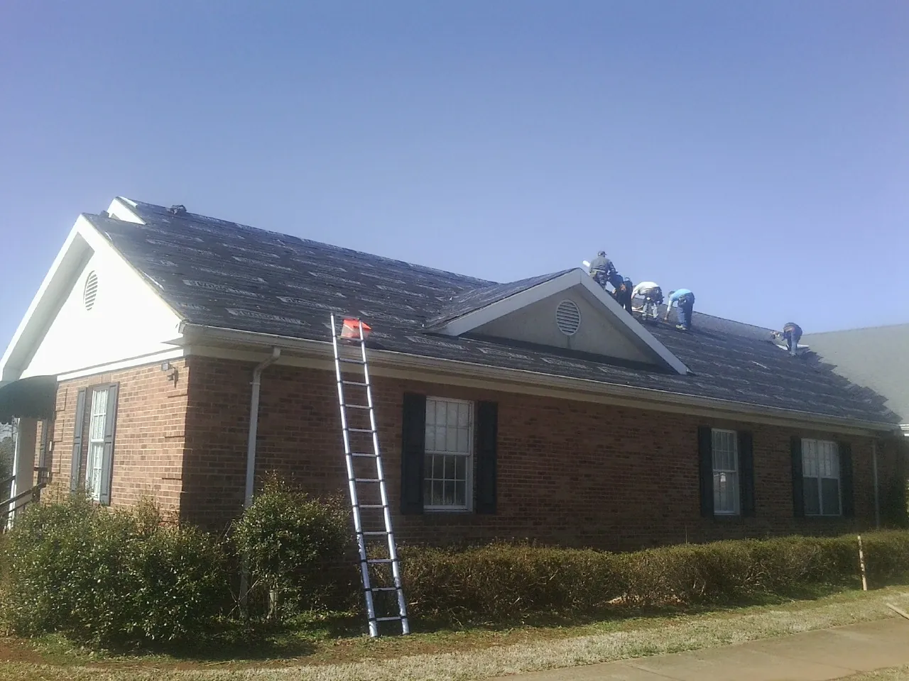 Crew tearing shingles off a brick ranch roof with a ladder set — Emergency Roof Repair work by our crew in Rydal