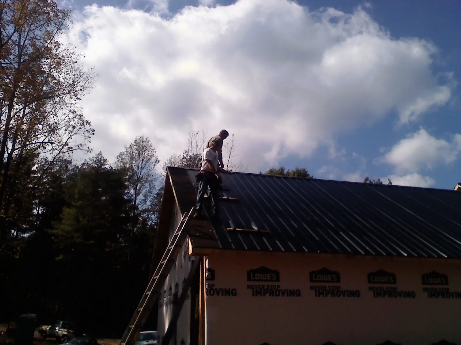 Roofer fastening dark metal panels high against a cloudy sky, from a Roof Inspection job in Rydal
