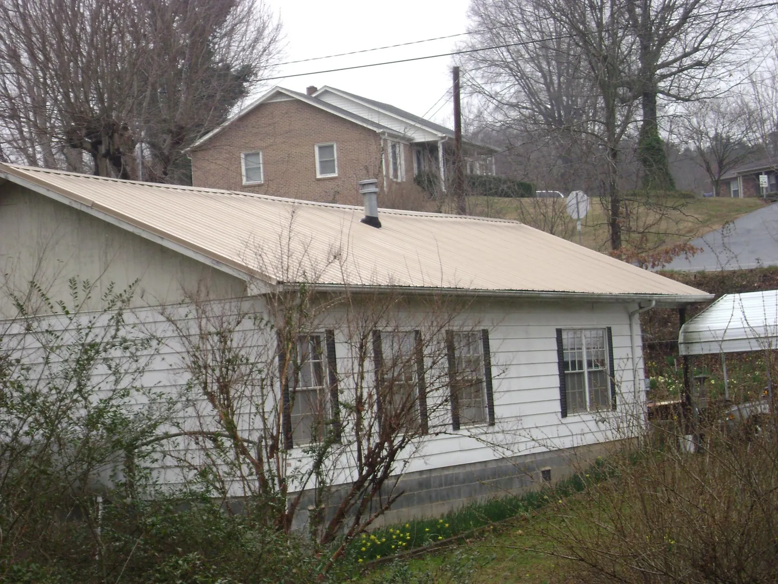 Tan metal roof on a white sided house set into a hillside — Commercial Roofing by Roofing Brothers in Rydal